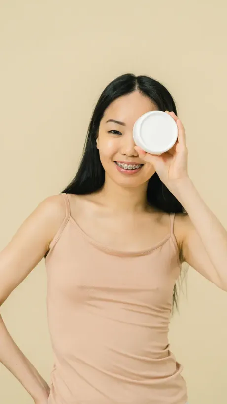 A creator holding a jar of moisturiser up beside her face, talking to camera.