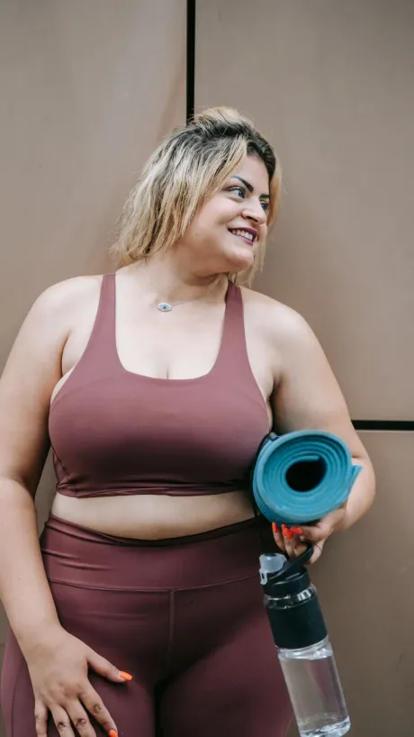 A creator holding a rolled yoga mat and a water bottle, talking to camera.