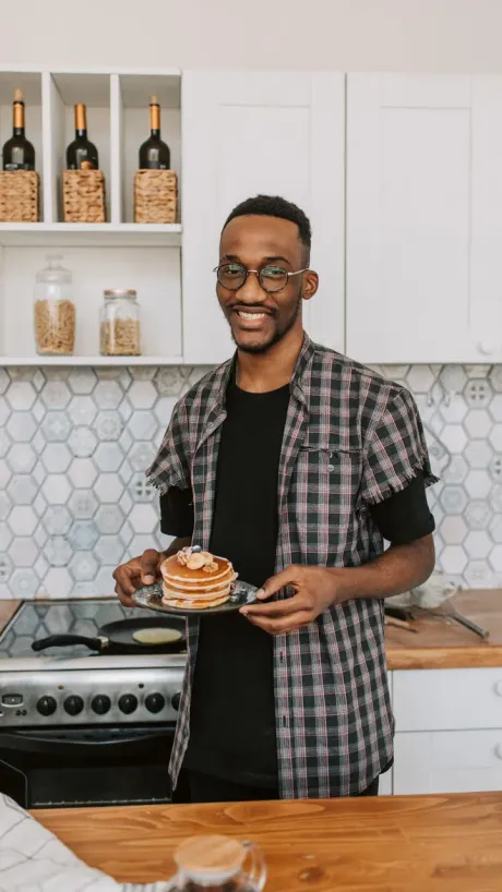 A creator in a kitchen holding a plate of pancakes up to camera.